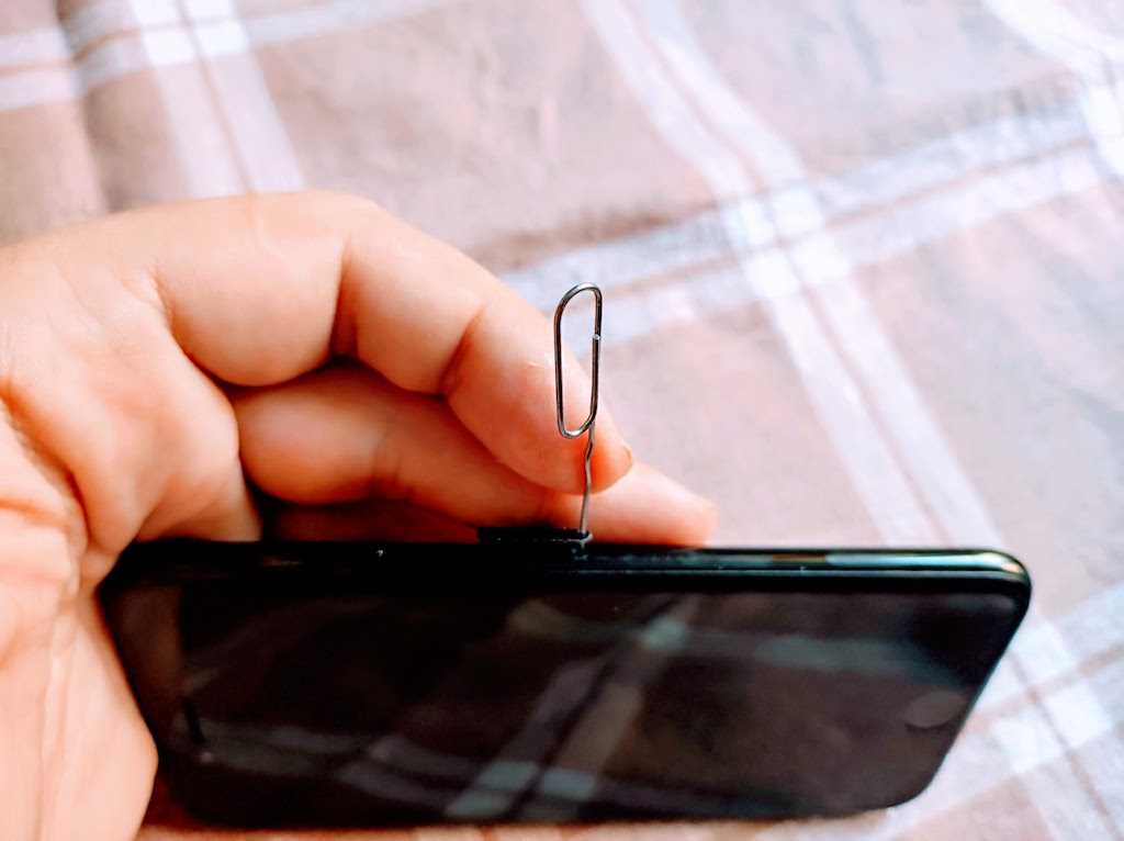 Затем найдите лоток для SIM-карт на боковой панели телефона и вставьте конец скрепки в крошечное отверстие.